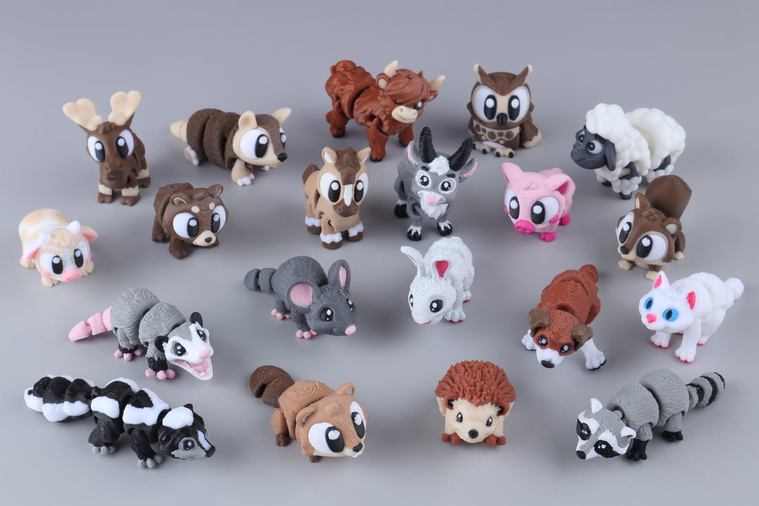 A set of small animal figurines arranged on a smooth gray surface. The collection includes a reindeer, brown bear, horse, sheep, owl, pig, goat, mouse, opossum, rabbit, dog, cat, skunk, hedgehog, and raccoon, each with cute cartoon-style features.
