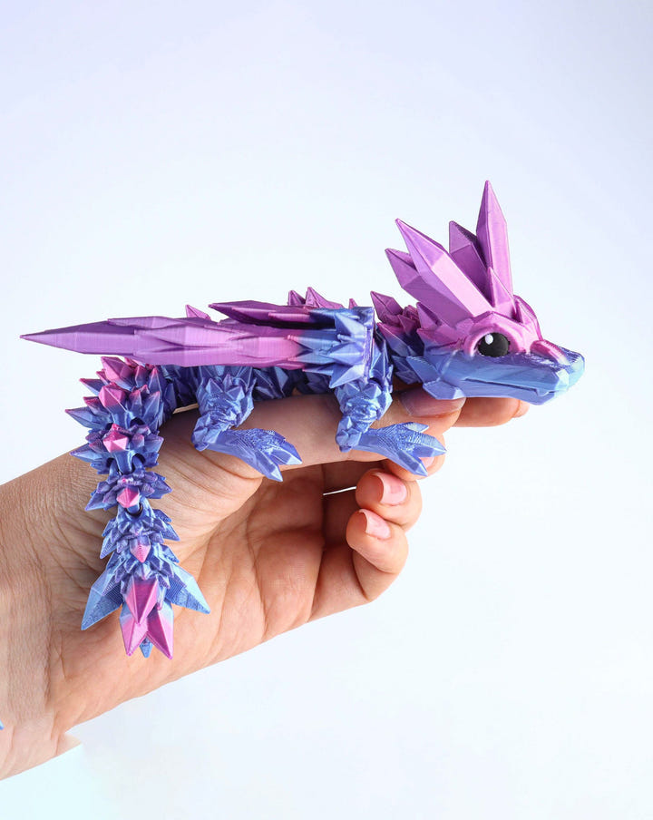 Hand holding a purple and blue dragon toy against a white background