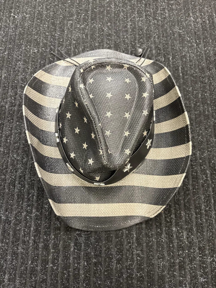 A cowboy hat featuring a black and beige horizontal stripe pattern on the brim and crown, with beige stars on a black background on the crown, photographed on a dark gray ribbed fabric background.