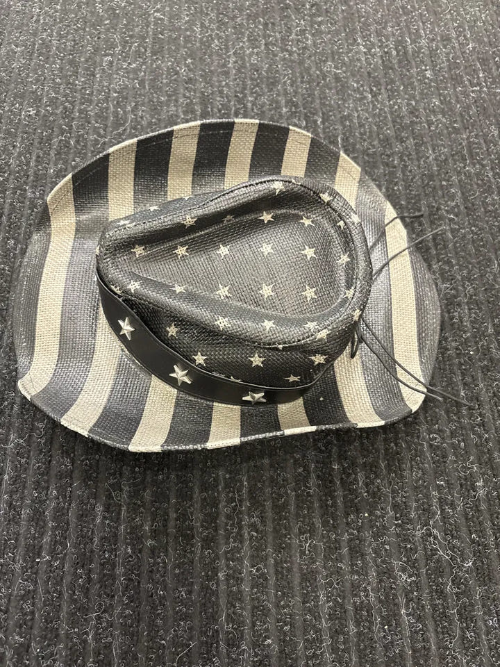 A small cowboy-style hat with black and cream stripes on the brim and a black crown patterned with small cream stars, placed on a dark ribbed fabric background.