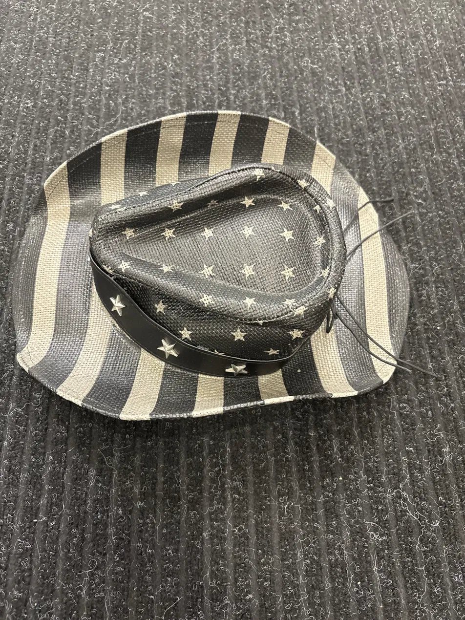 A small cowboy-style hat with black and cream stripes on the brim and a black crown patterned with small cream stars, placed on a dark ribbed fabric background.