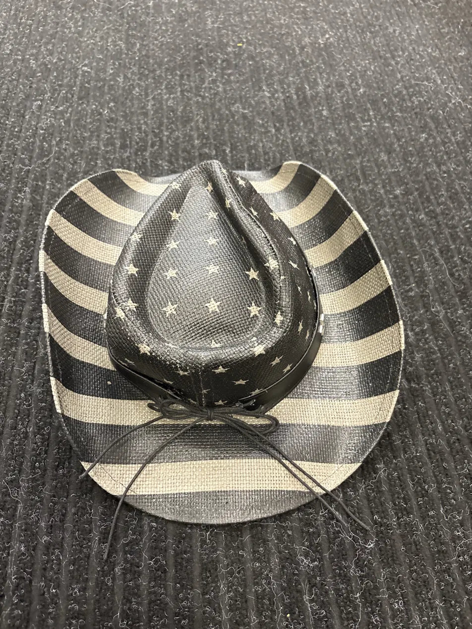 A cowboy hat with a black and beige striped brim and a black crown decorated with beige stars, resting on a dark textured surface.
