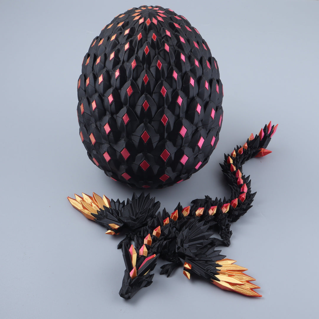 A black dragon figurine with metallic gold and red accents lies in front of a matching black dragon egg decorated with red diamond-shaped inlays, set against a solid gray background.