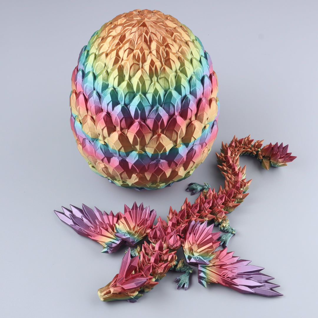 A colorful origami dragon and matching egg displayed on a light gray background. The dragon is made of iridescent, rainbow-finished paper with pink, purple, blue, green, and gold tones, while the egg has a striped pattern of the same metallic colors.