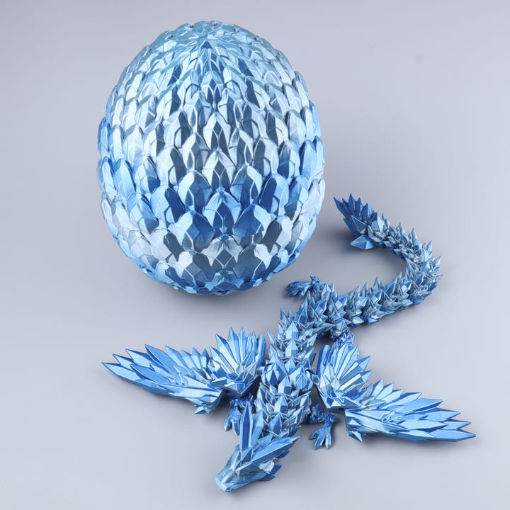 A metallic blue dragon figurine with a faceted, geometric scale texture, shown with a matching blue egg-shaped container on a light gray background.