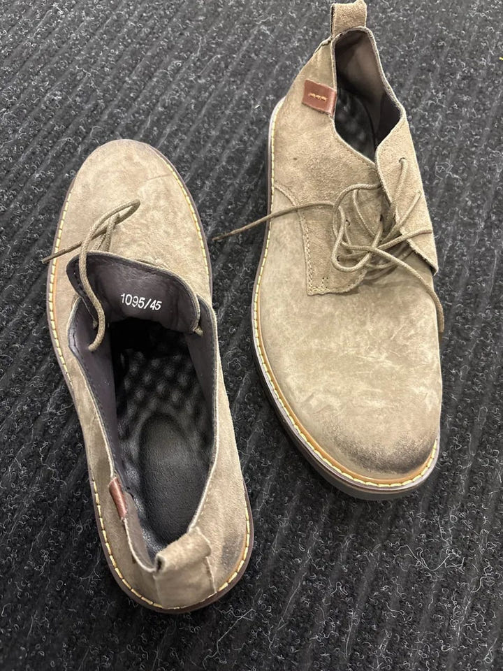 A pair of light beige suede lace-up ankle boots shown from the top and side on a dark textured carpet.