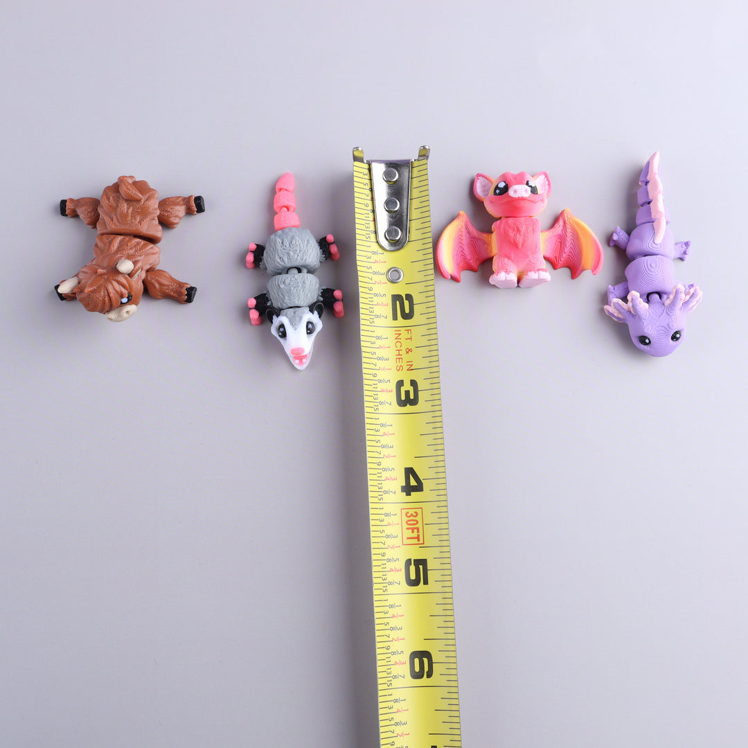 Four small animal figurines next to a measuring tape on a light gray background