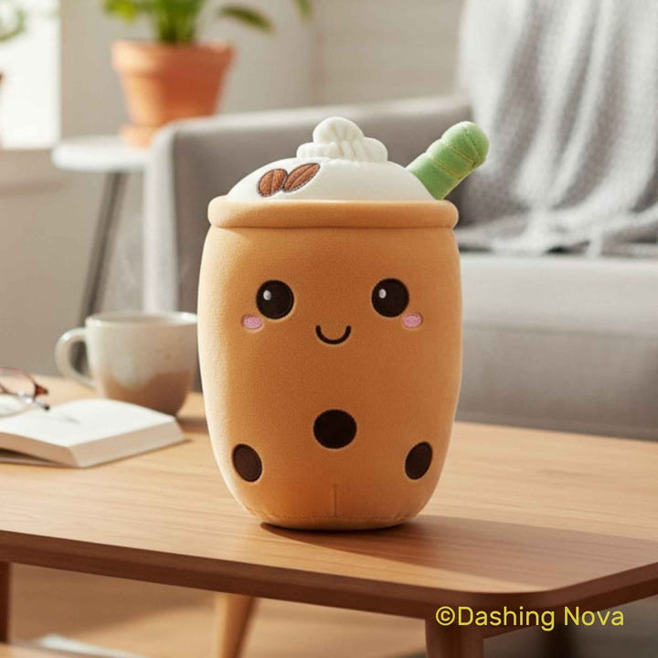A cute, smiling boba drink character plush toy sits on a wooden table in a cozy, softly blurred living room setting. The plush is designed to look like a bubble tea cup with a cream-colored lid topped with whipped cream and two coffee beans, a green straw, and black bubble dots on the body.