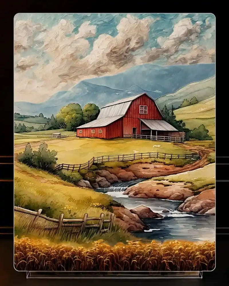 A vertical metal print of  landscape art print depicting a red barn, a winding stream, and rolling green hills under a cloudy blue sky, displayed on a clear acrylic stand.